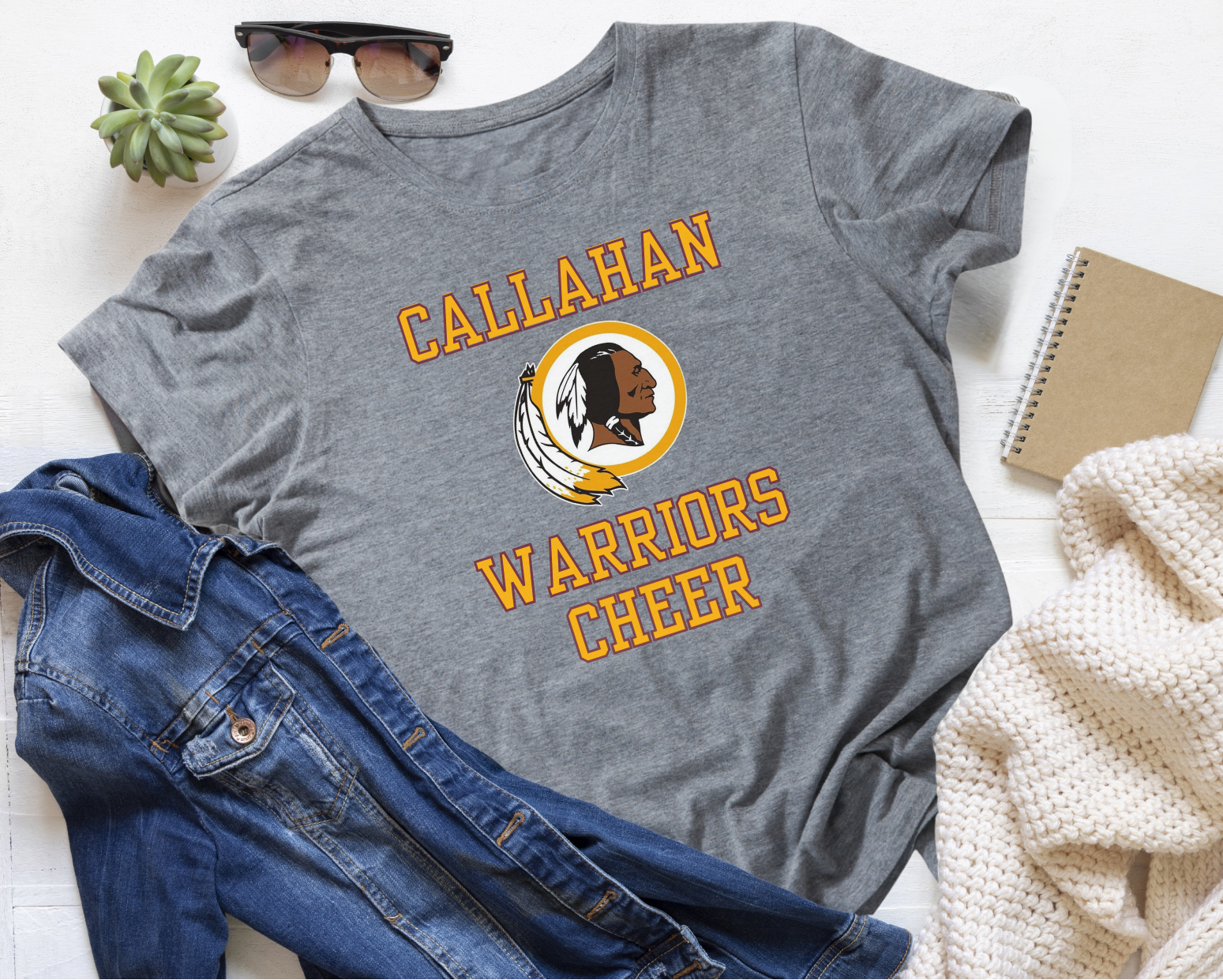 Gray t-shirt with 'Callahan Warriors Cheer' design on a white surface with jeans and sunglasses.