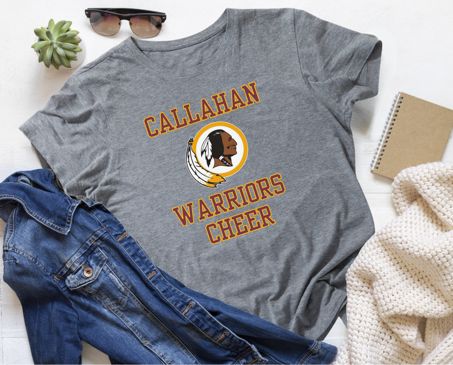 Gray t-shirt with 'Callahan Warriors Cheer' design on a white surface with jeans and sunglasses.