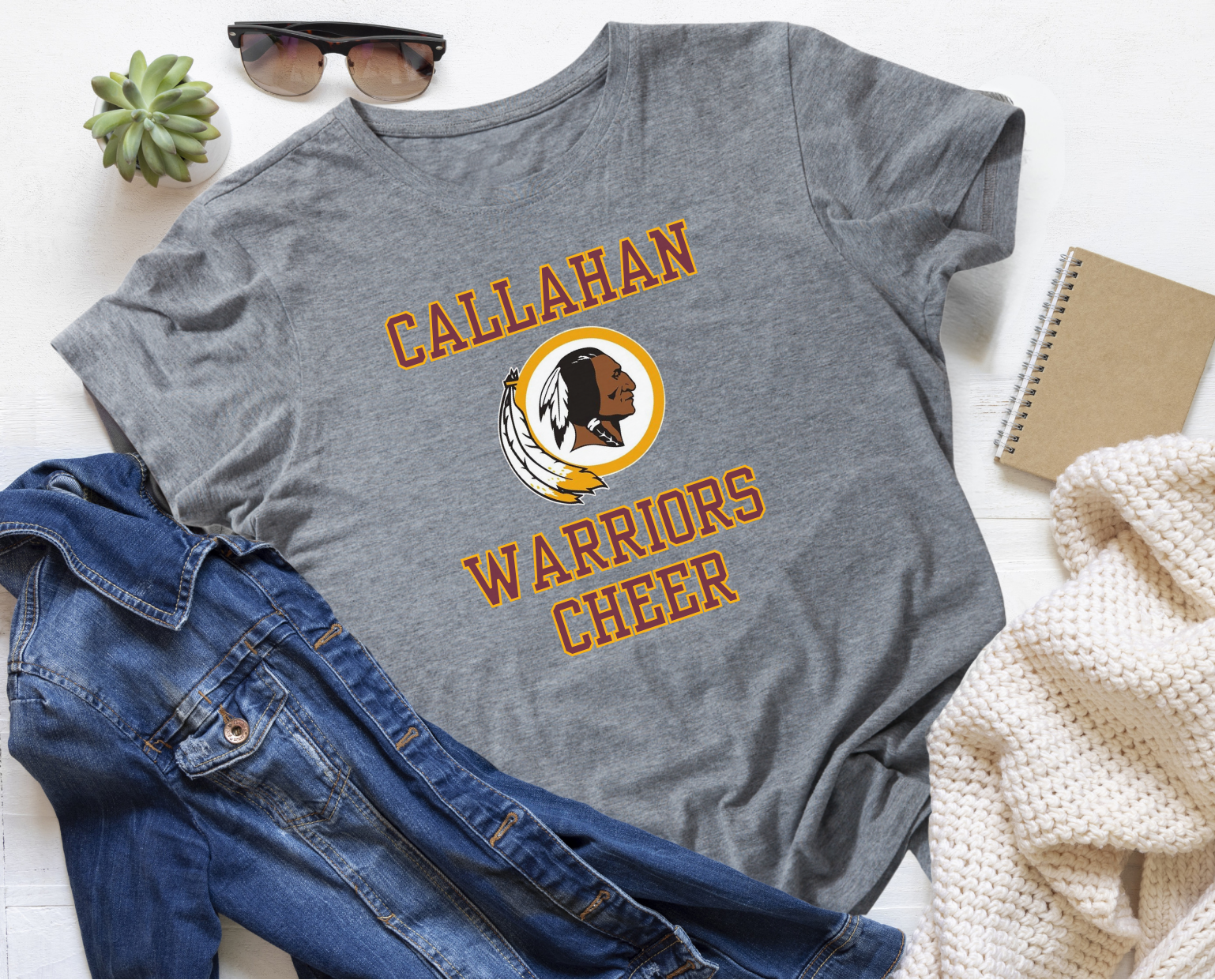 Gray t-shirt with 'Callahan Warriors Cheer' design on a white surface with jeans and sunglasses.
