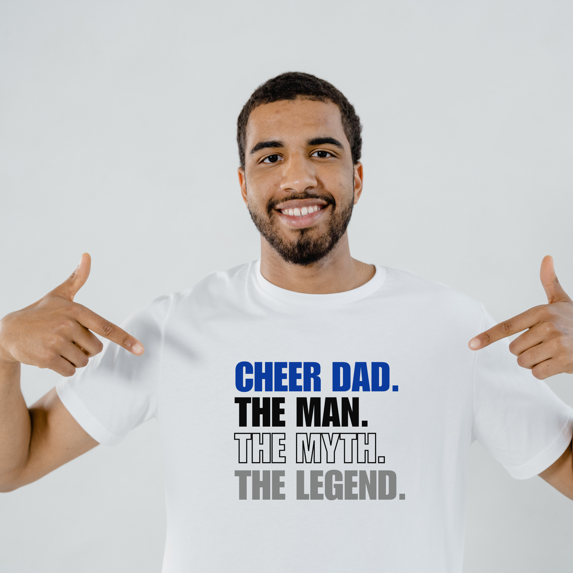 Man wearing a white t-shirt with 'CHEER DAD. THE MAN. THE MYTH. THE LEGEND.' text, pointing at the shirt.